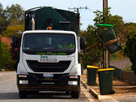 A SOLO rubbish truck lifts up a kerbside rubbish bin.