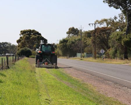 A tractor slashes tall grass on a country roadside, one of the ways council manages bushfire risk.